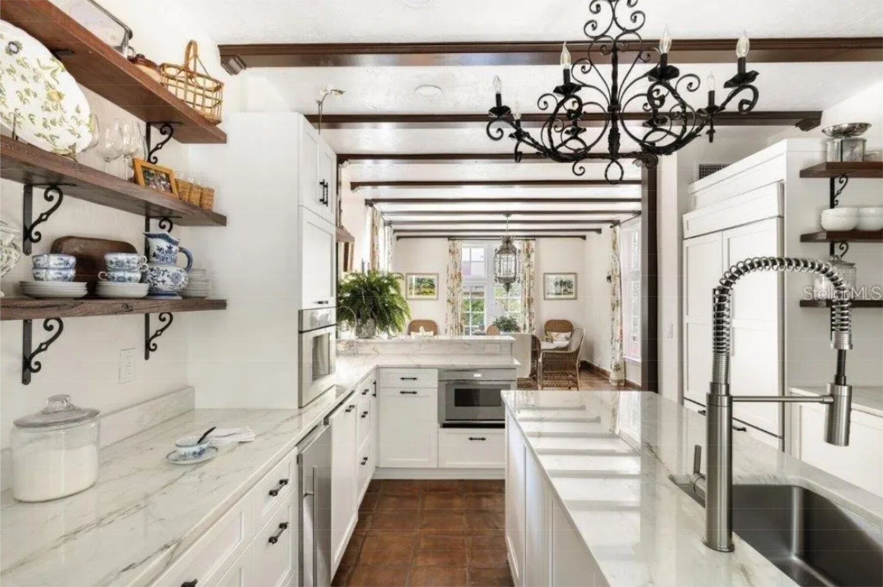 Kitchen looking down the aisle to a marble-topped island, built-in wall oven and wrought-iron chandelier