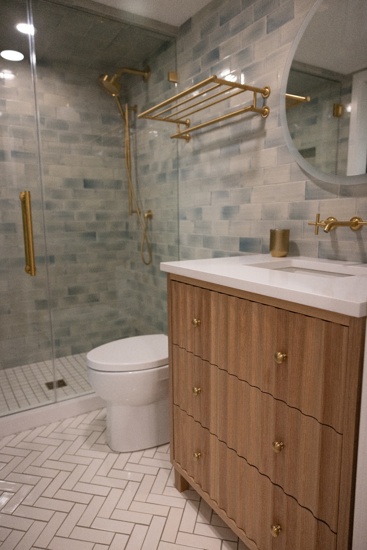 Bathroom vanity with blue tile shower and brass fixtures