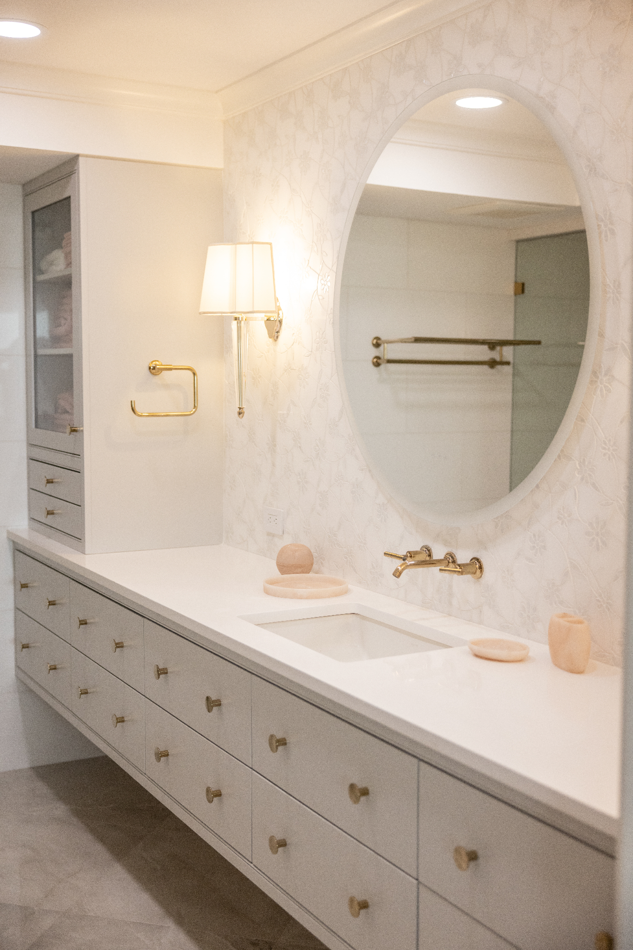 White floating vanity with brass fixtures and oval mirror