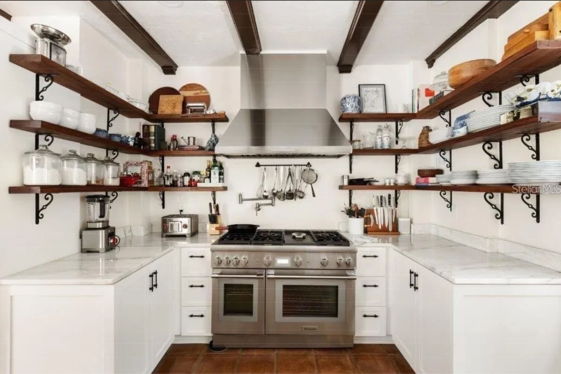 Kitchen with stainless range and hood, dark wood open shelving on black brackets and beamed ceiling