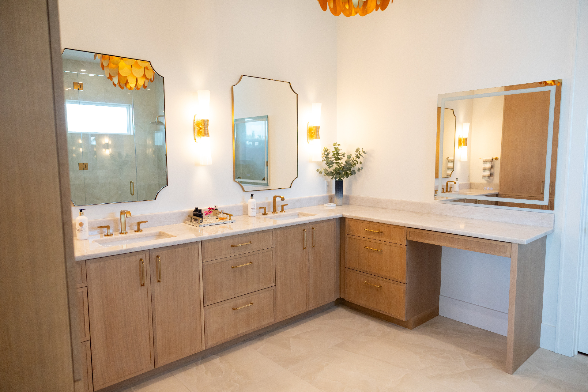 Light oak bathroom double vanity with marble countertops and brass fixtures